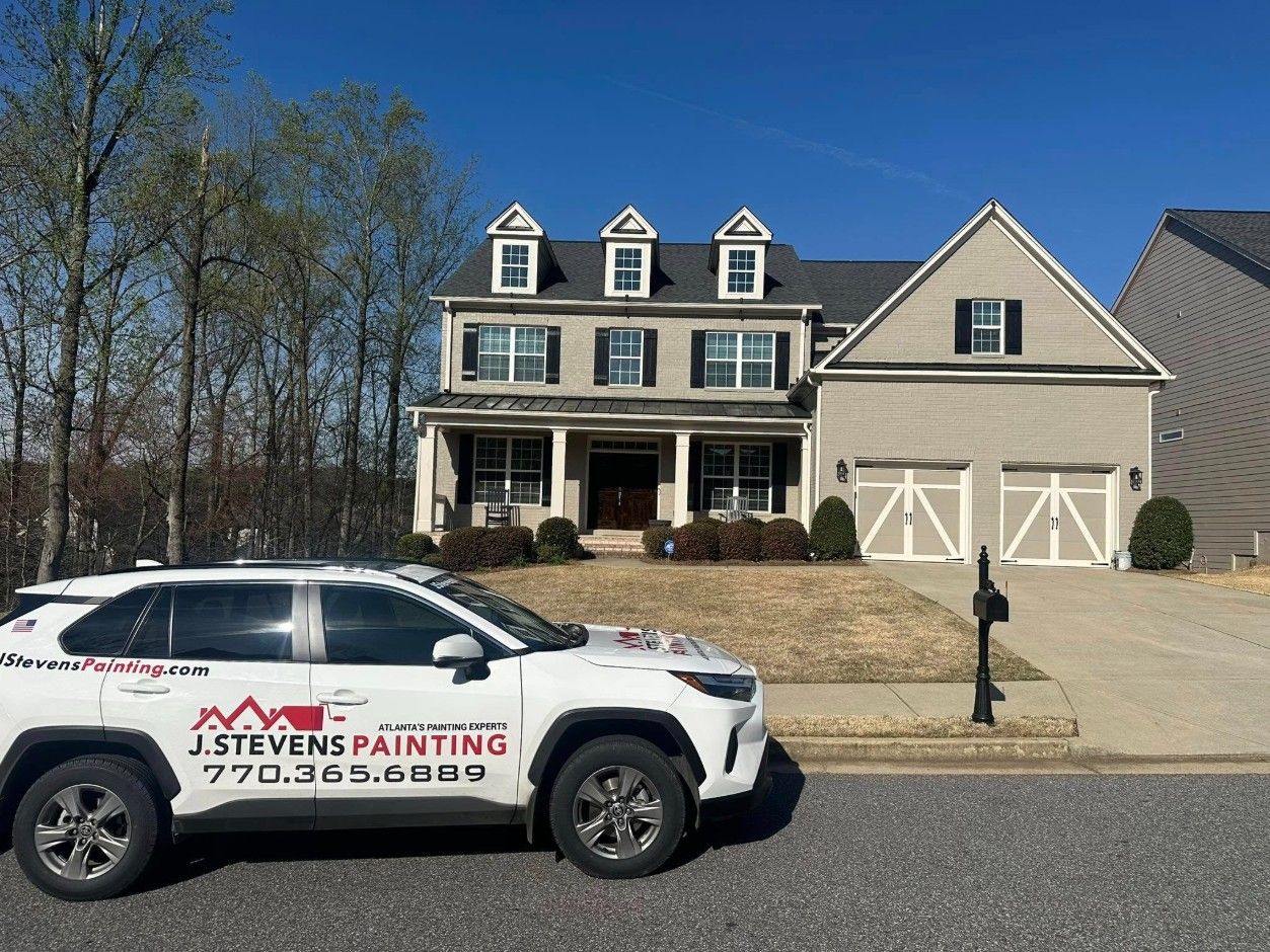 Gray painted brick home with black shutters and cream carriage garage doors