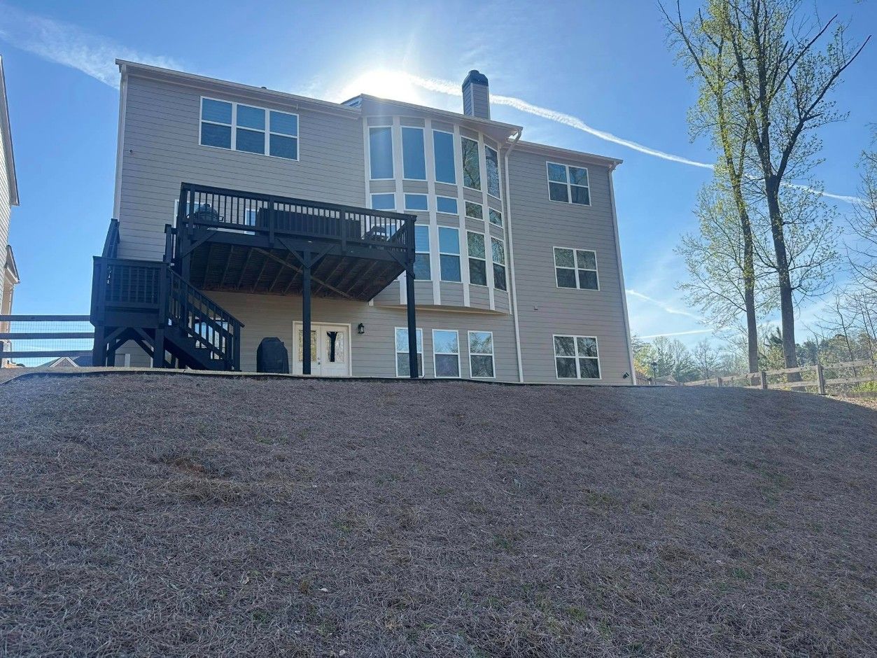 Rear of a three-story tan home with a dark-stained deck